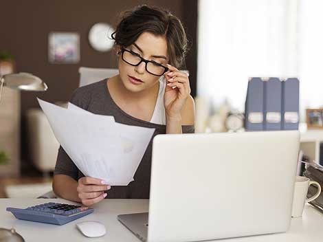Frau mit Brille sitz vor Ihrem Laptop und prüft Unterlagen © Fotolia.com, gpointstudio Frau mit Brille sitz vor Ihrem Laptop und prüft Unterlagen