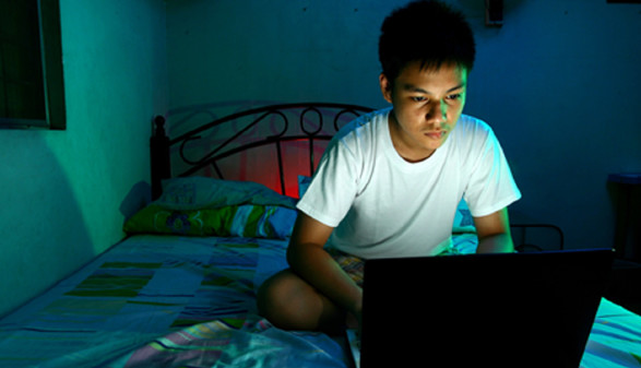 Jugendlicher mit Laptop auf dem Bett